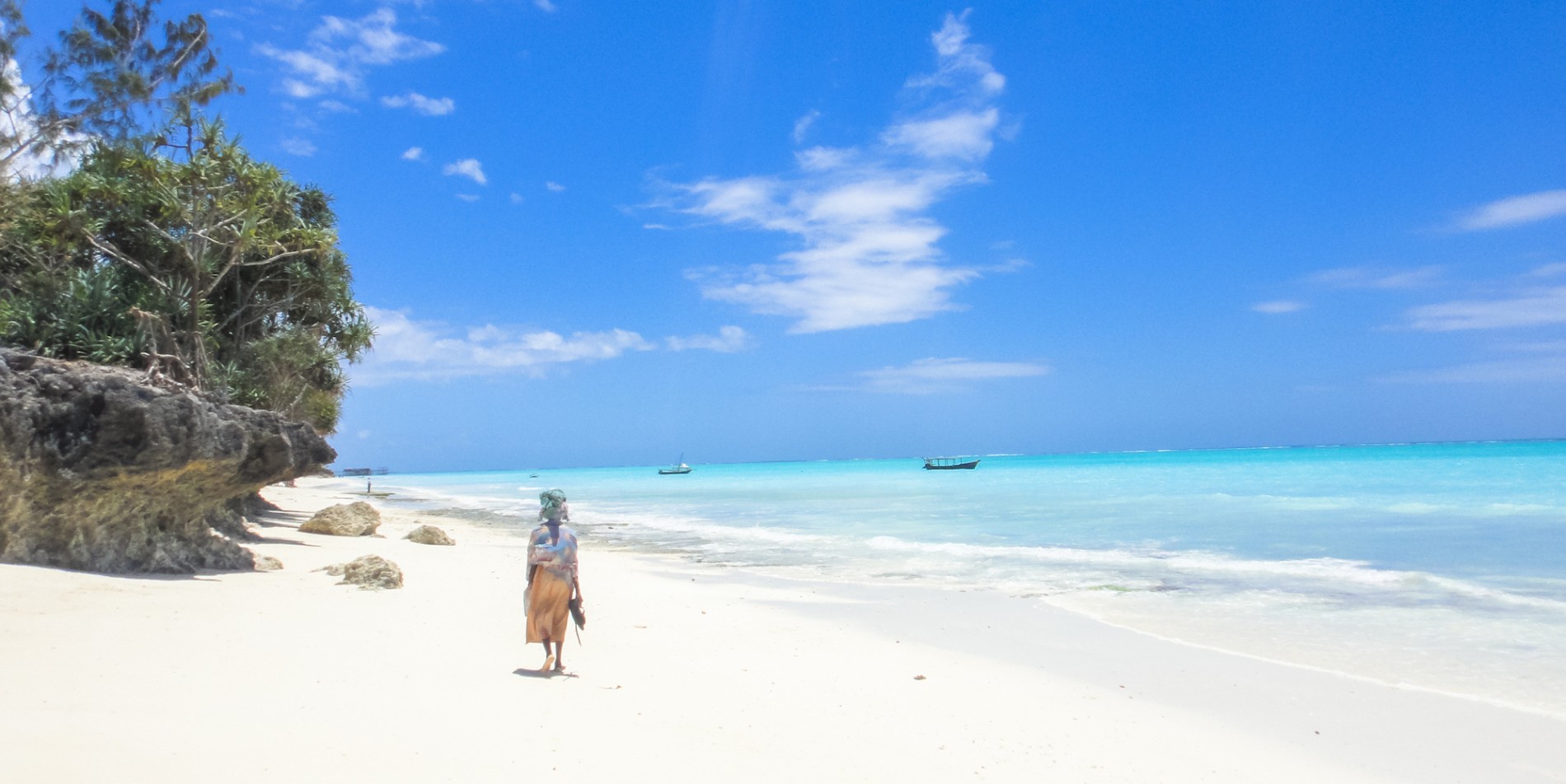 A person walking down a remote beach with white sand and crystal clear water in Eastern Africa