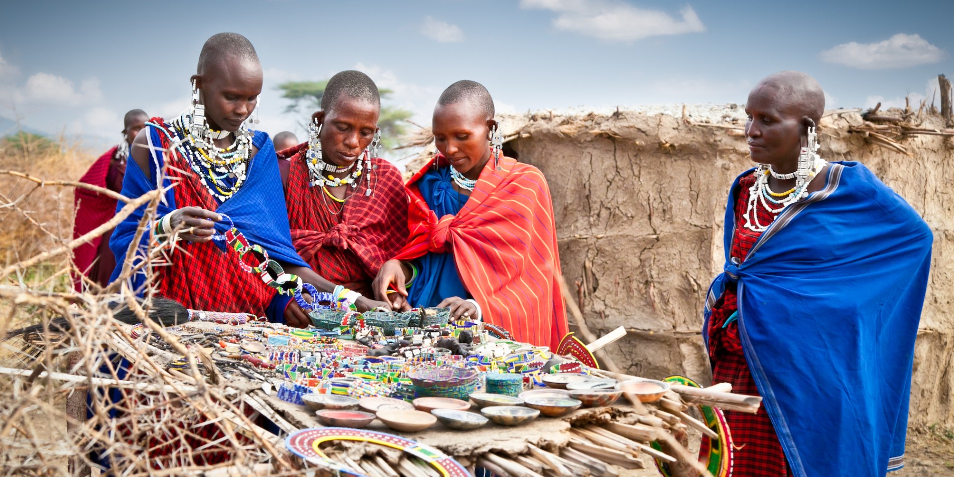 Four people of the Masai tribe in Tanzania gather around traditional art and ornaments in a village in Tanzania