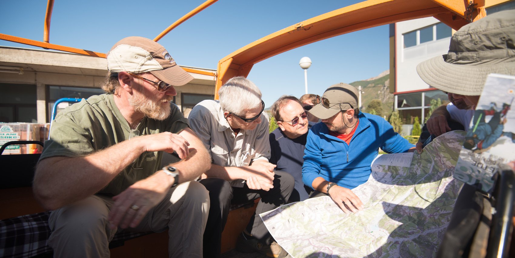 A group of men sitting in an open car looking at a map and devising a plan all together