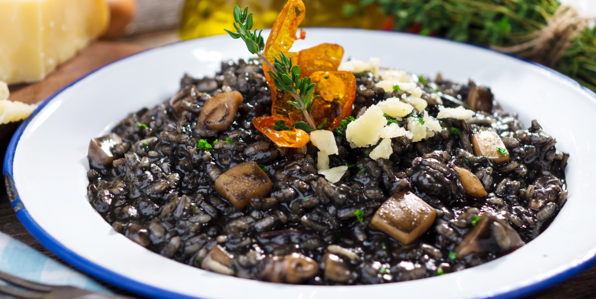Squid ink black risotto topped with an orange leaf on a white plate