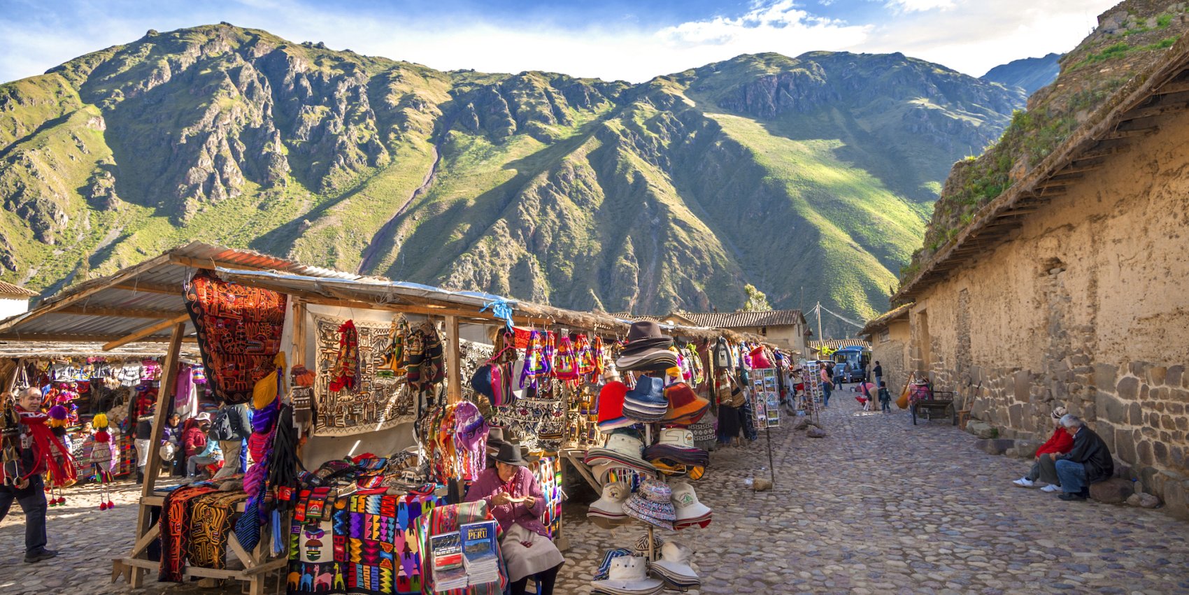 A colorful craft market in Peru with grassy mountains in the background on a sunny day.