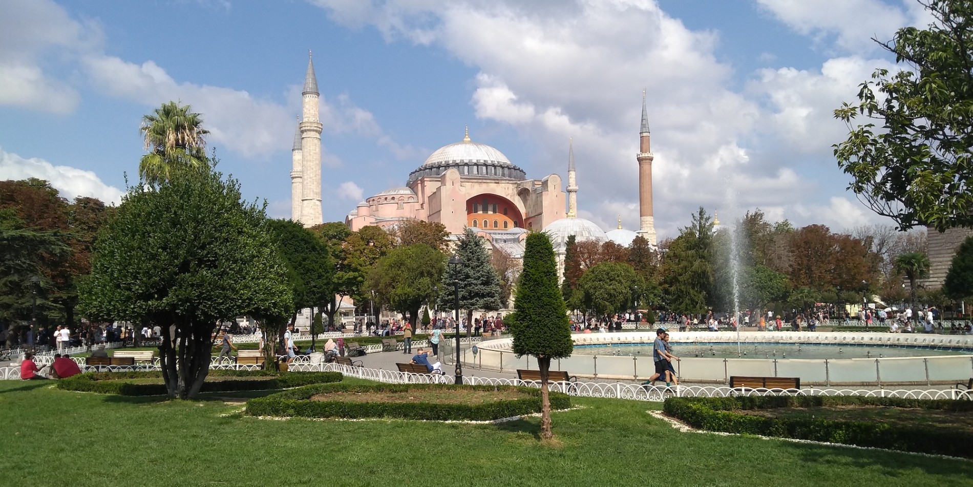 View if Hagia Sophia and surrounding park and fountain with people walking around on a sunny day in Turkey