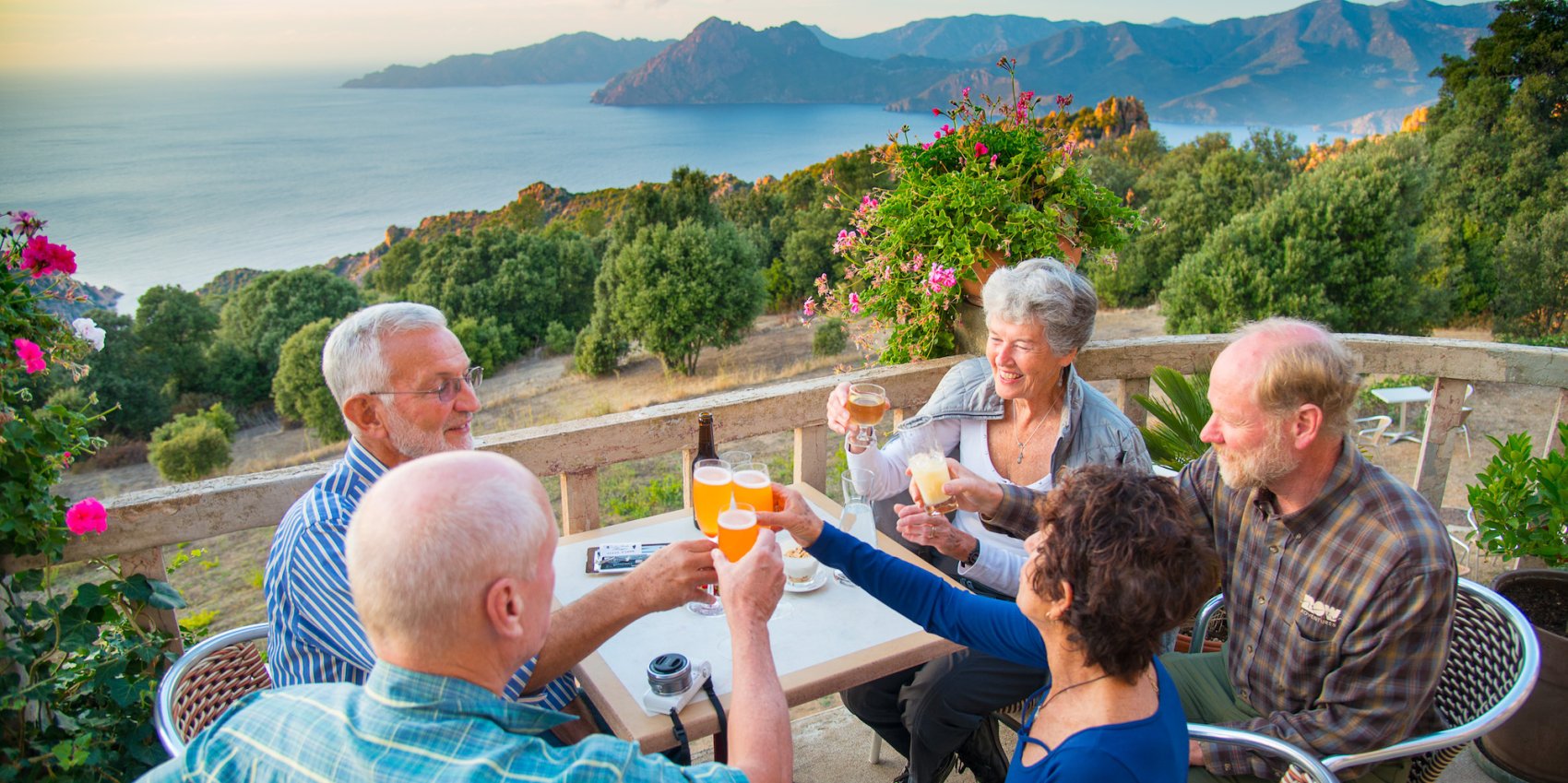 People sitting around a table raising a glass while smiling at sunset at a rooftop restaurant in Corsica, France.