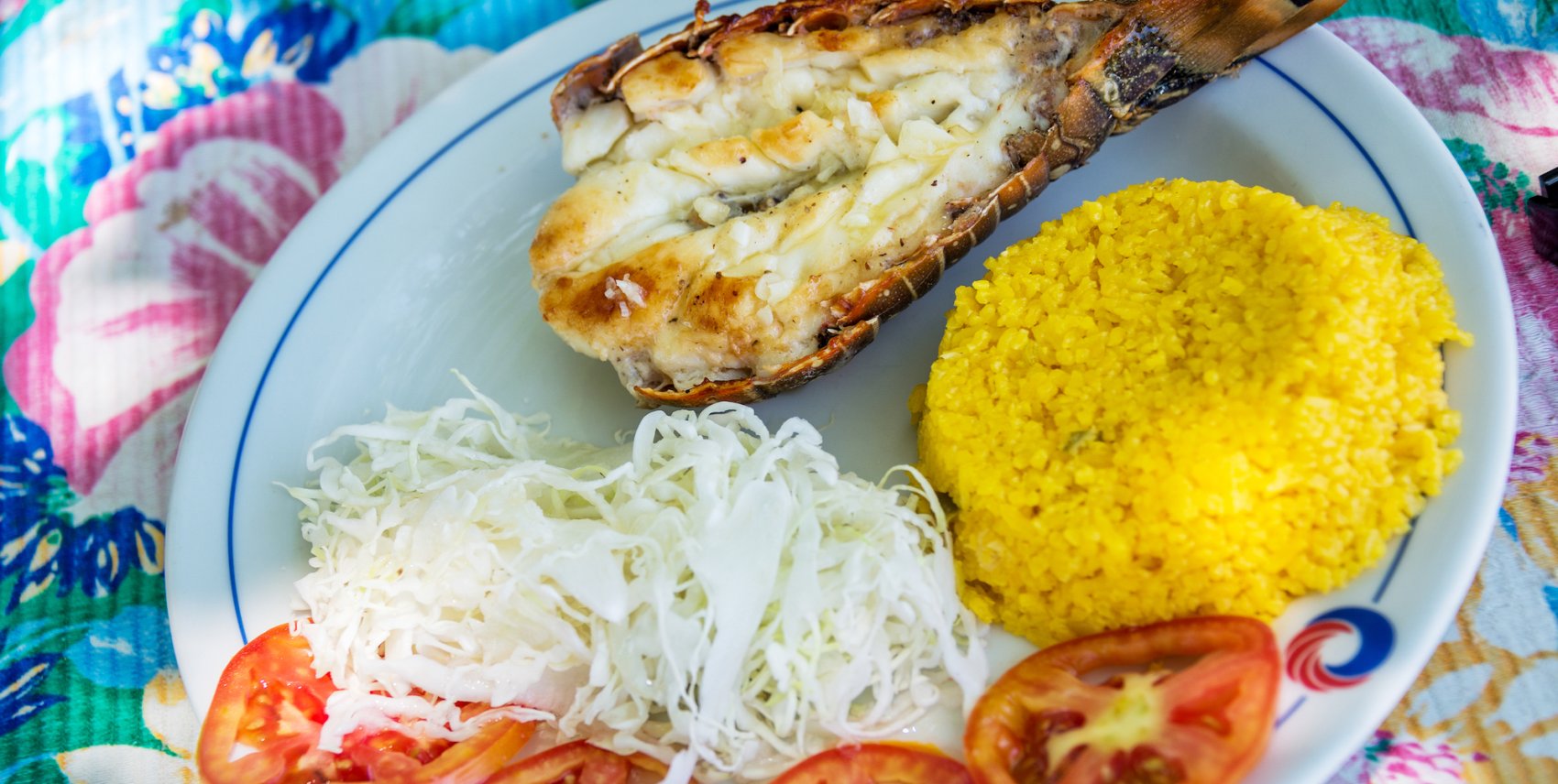 Fish, rice, noodles, and slices of tomato on a white plat atop a colorful table cloth in Cuba