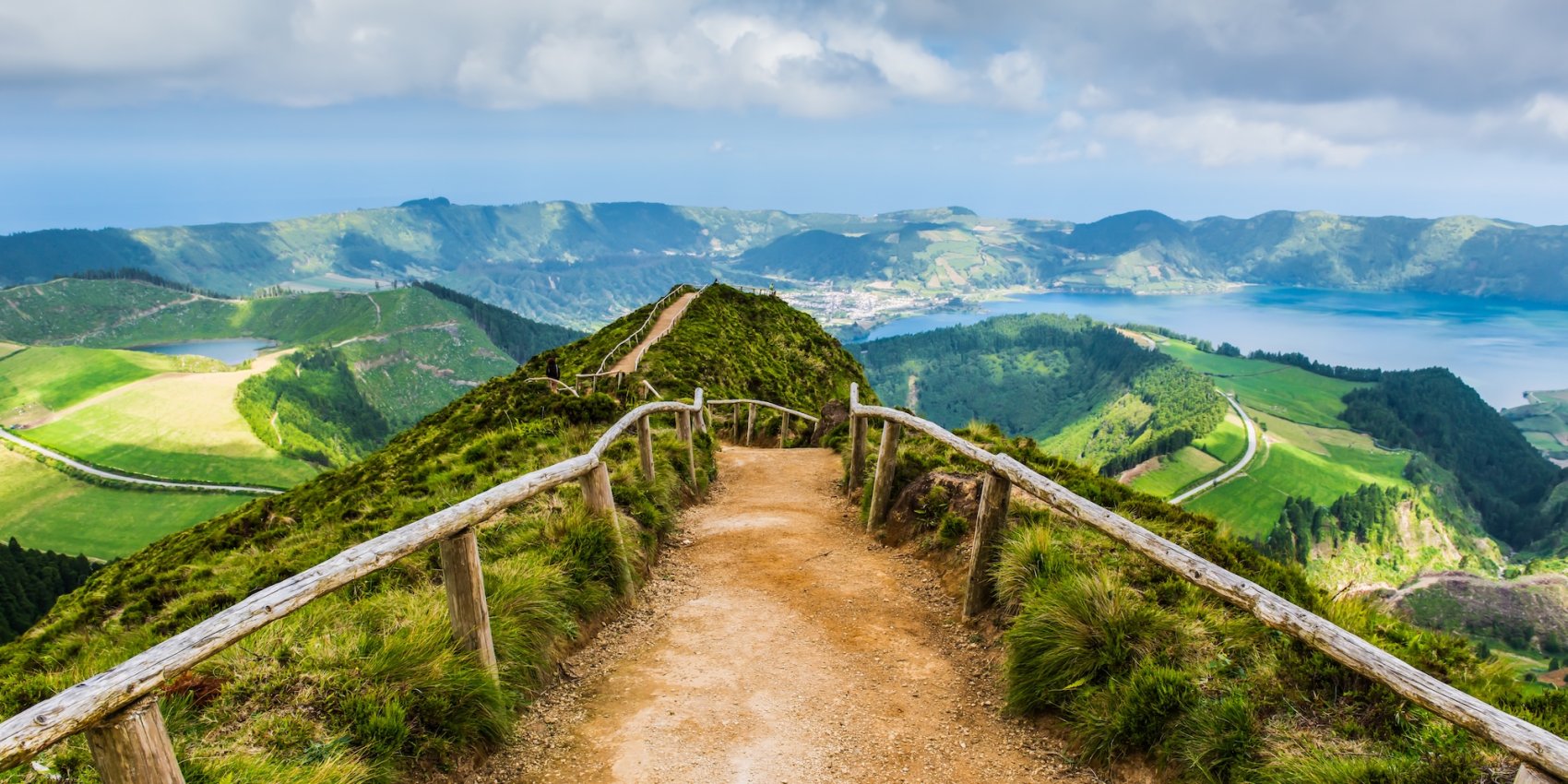 Scenic ridgeline trail on São Miguel Island in the Azores, with a dirt path leading through lush green hills overlooking crater lakes and volcanic landscapes.