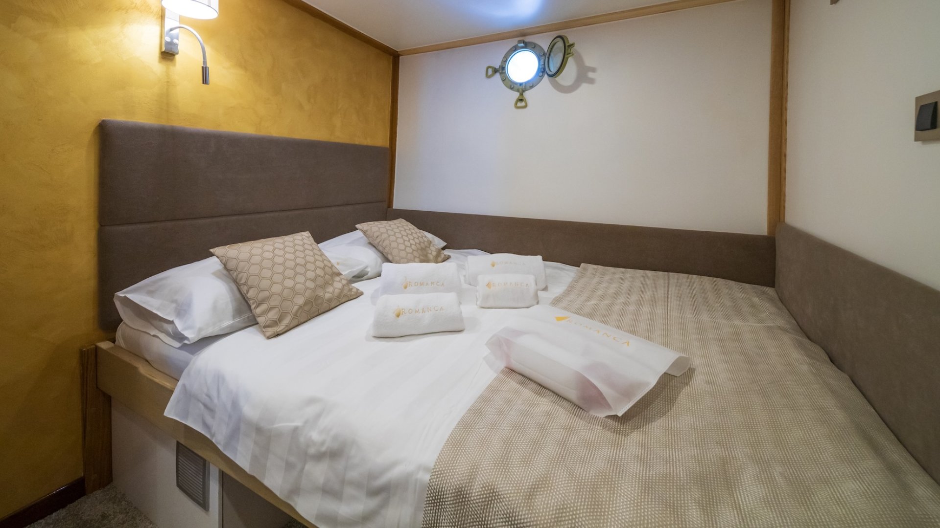 A cabin on a yacht in Croatia with a neatly made bed, towels, and a small window.