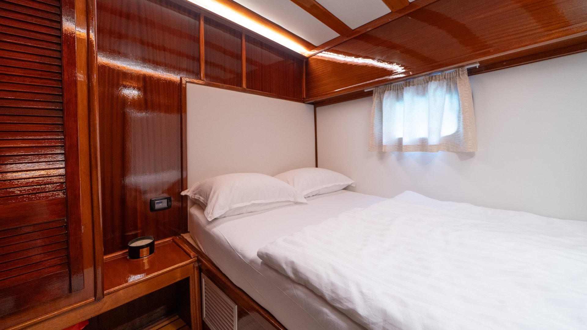 Yacht cabin with a neatly made bed, a side table, and small window.