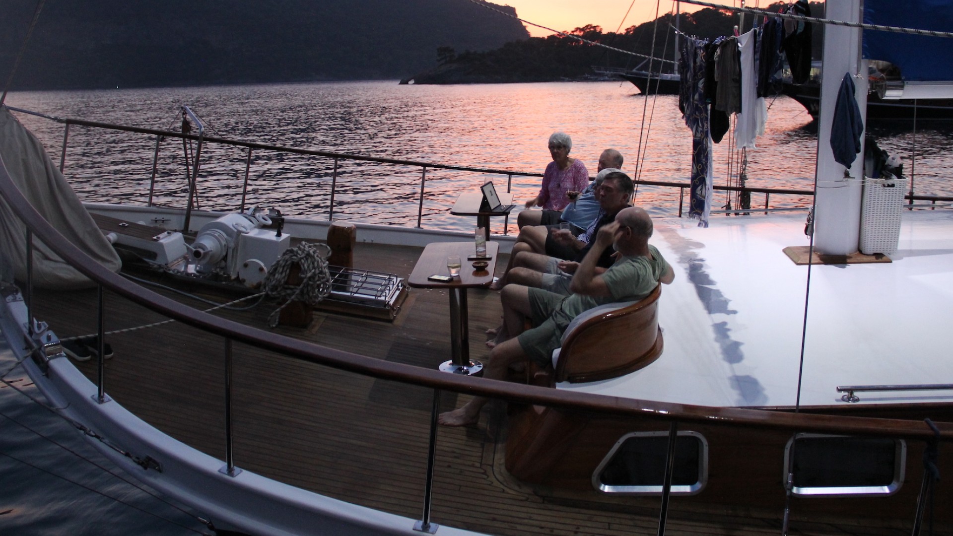 Group of tourists sitting on the bow of a yacht at sunset.