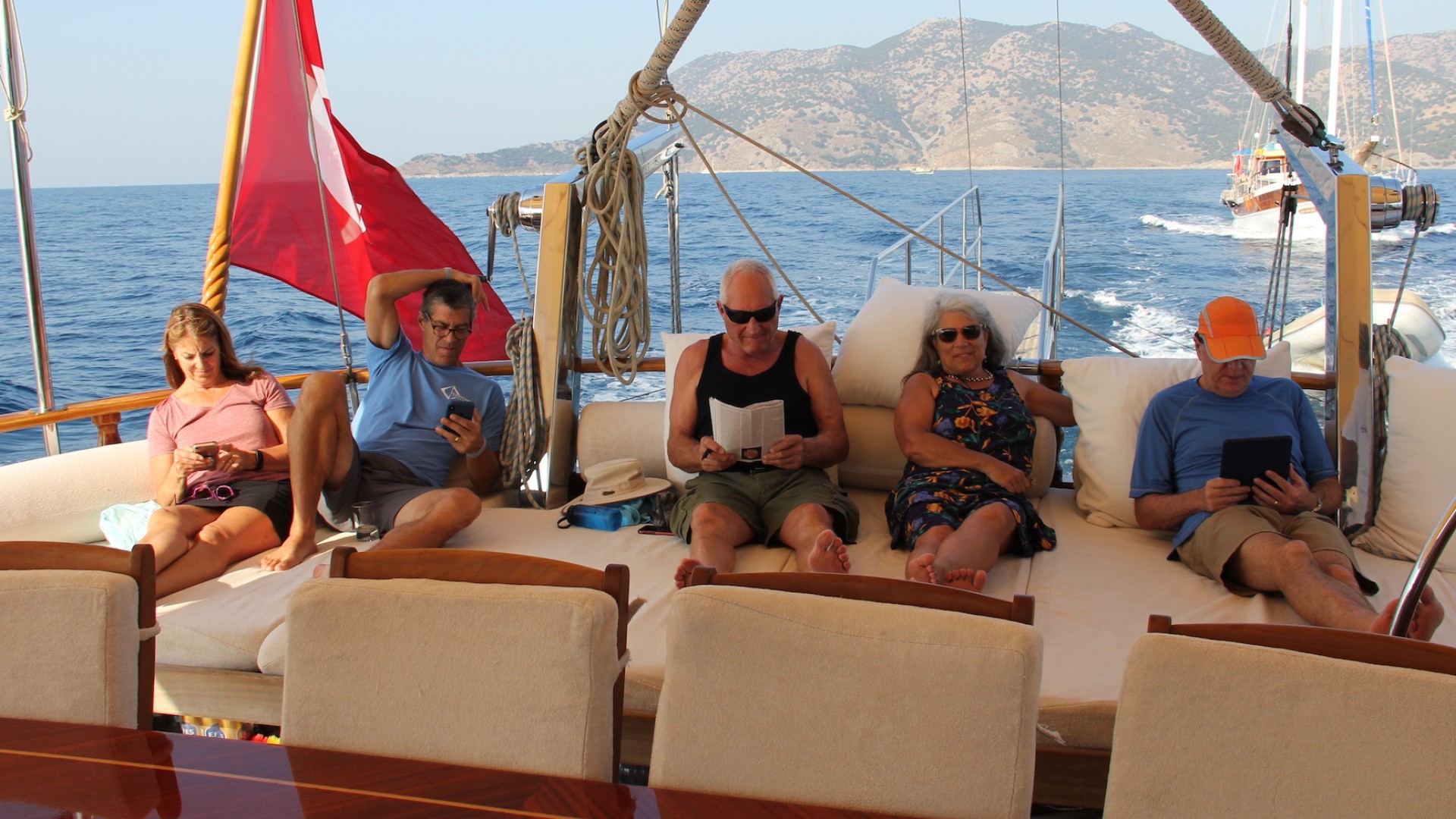 A group of people lounging under a shaded deck at the back of a small yacht in Turkey