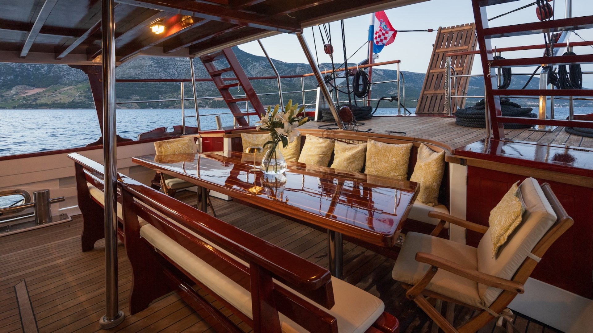An outdoor dining area on a yacht with a wooden table and cushioned seating.