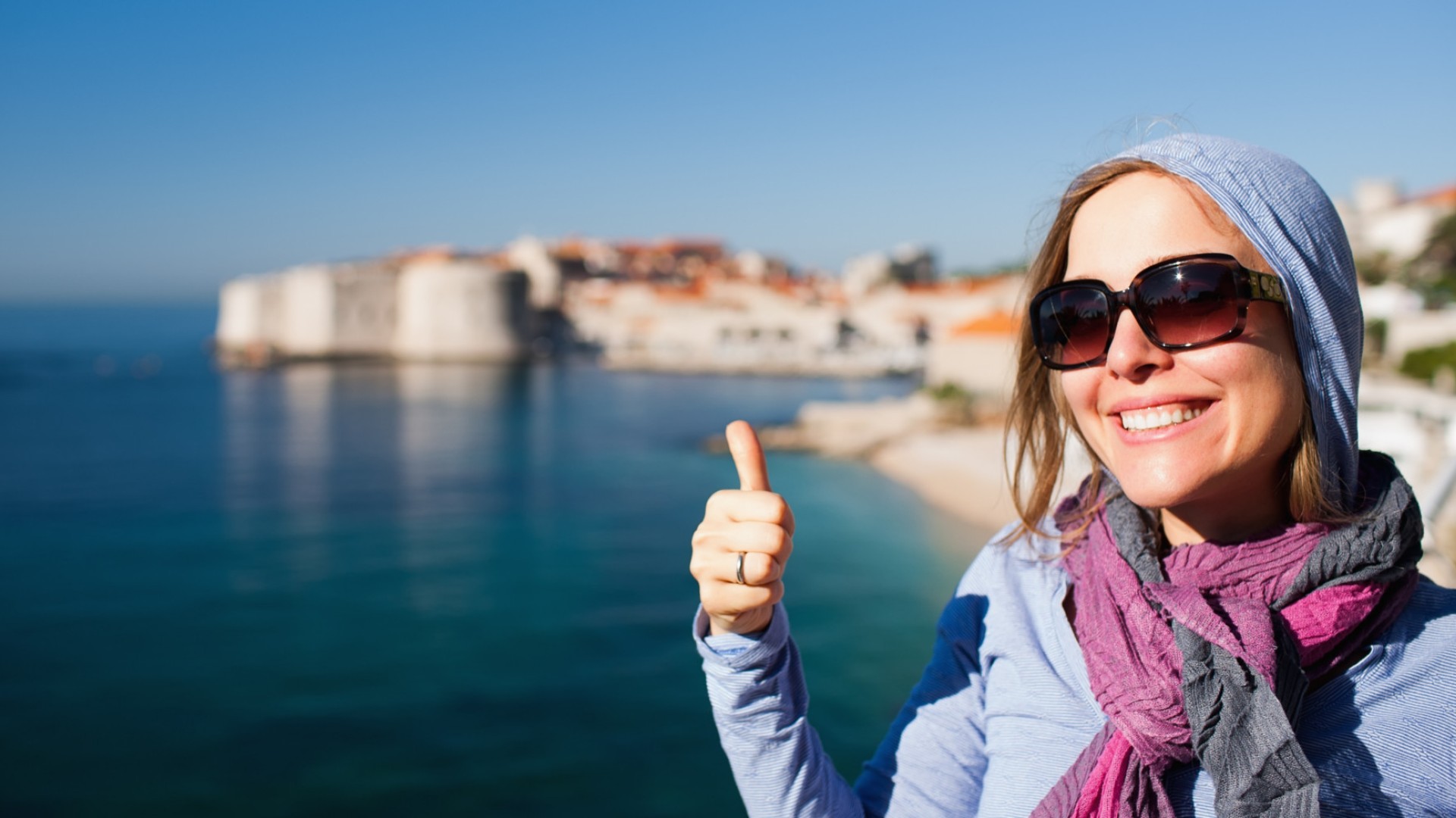 A woman wearing sunglasses smiling in the right third of the image in front of Adriatic Sea in Croatia