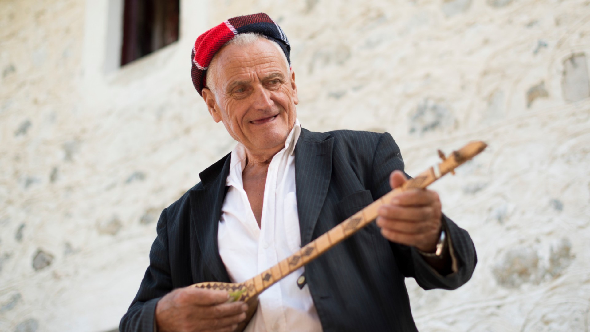 Albanian man wearing a colorful hat playing the guitar in the streets