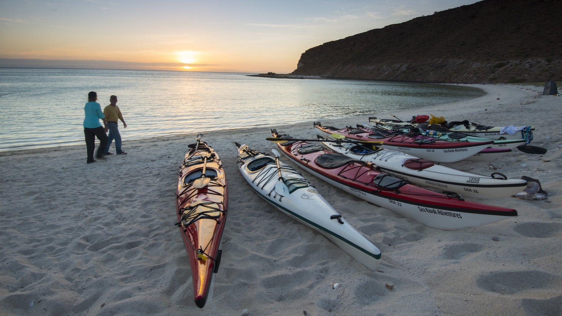 Person walking past a group of kayaks pulled up on the shore of Isla Espiritu Santo off of La Paz
