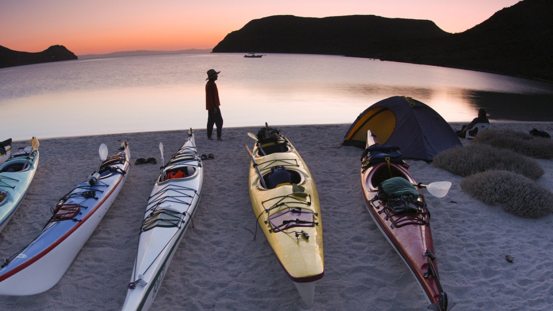 Person walking past a group of kayaks pulled up on the shore of an island in Loreto Bay National Marine Park