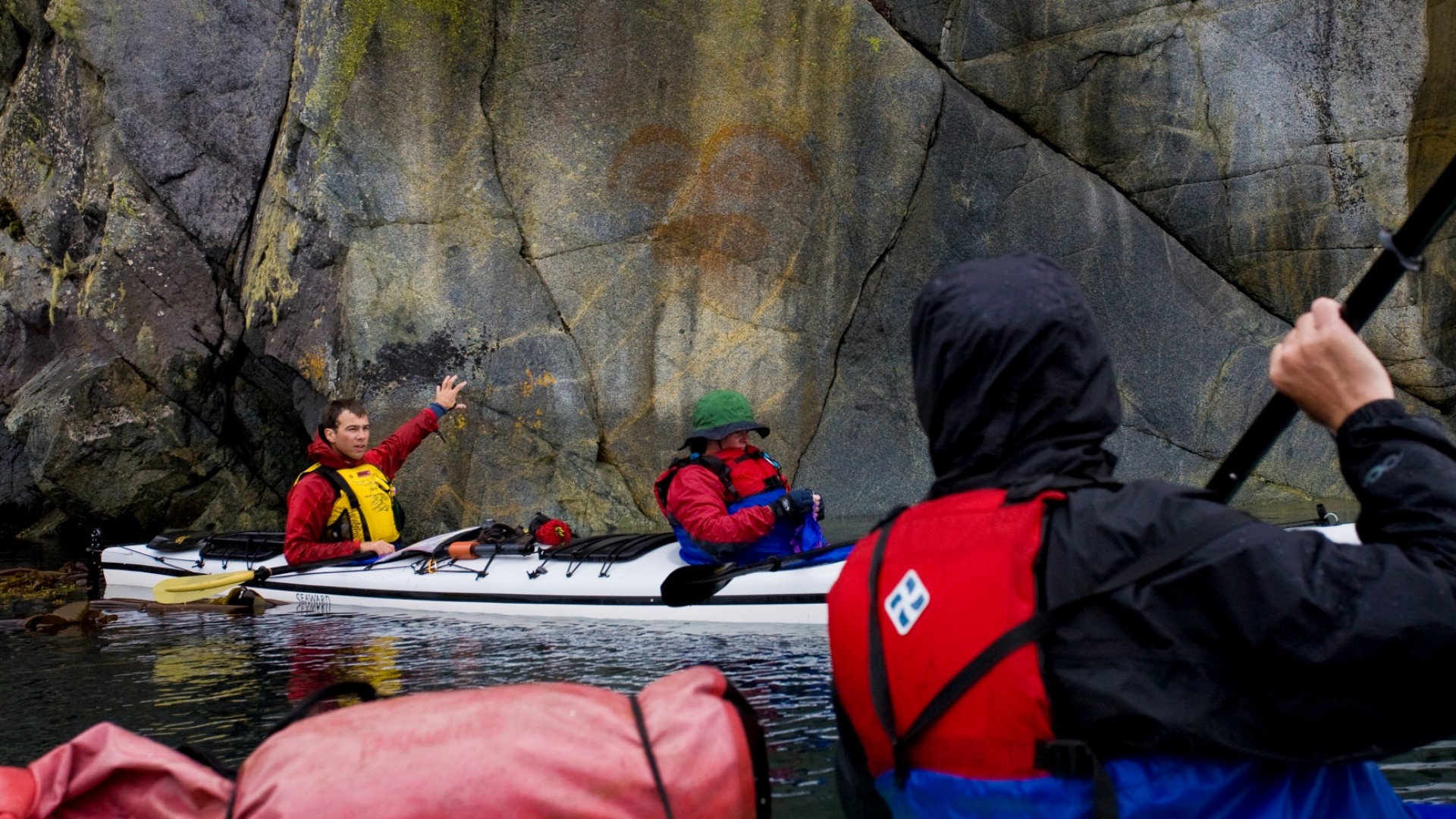 A group of sea kayakers paddling past Berry Island and admiring a pictograph on a boulder along the water