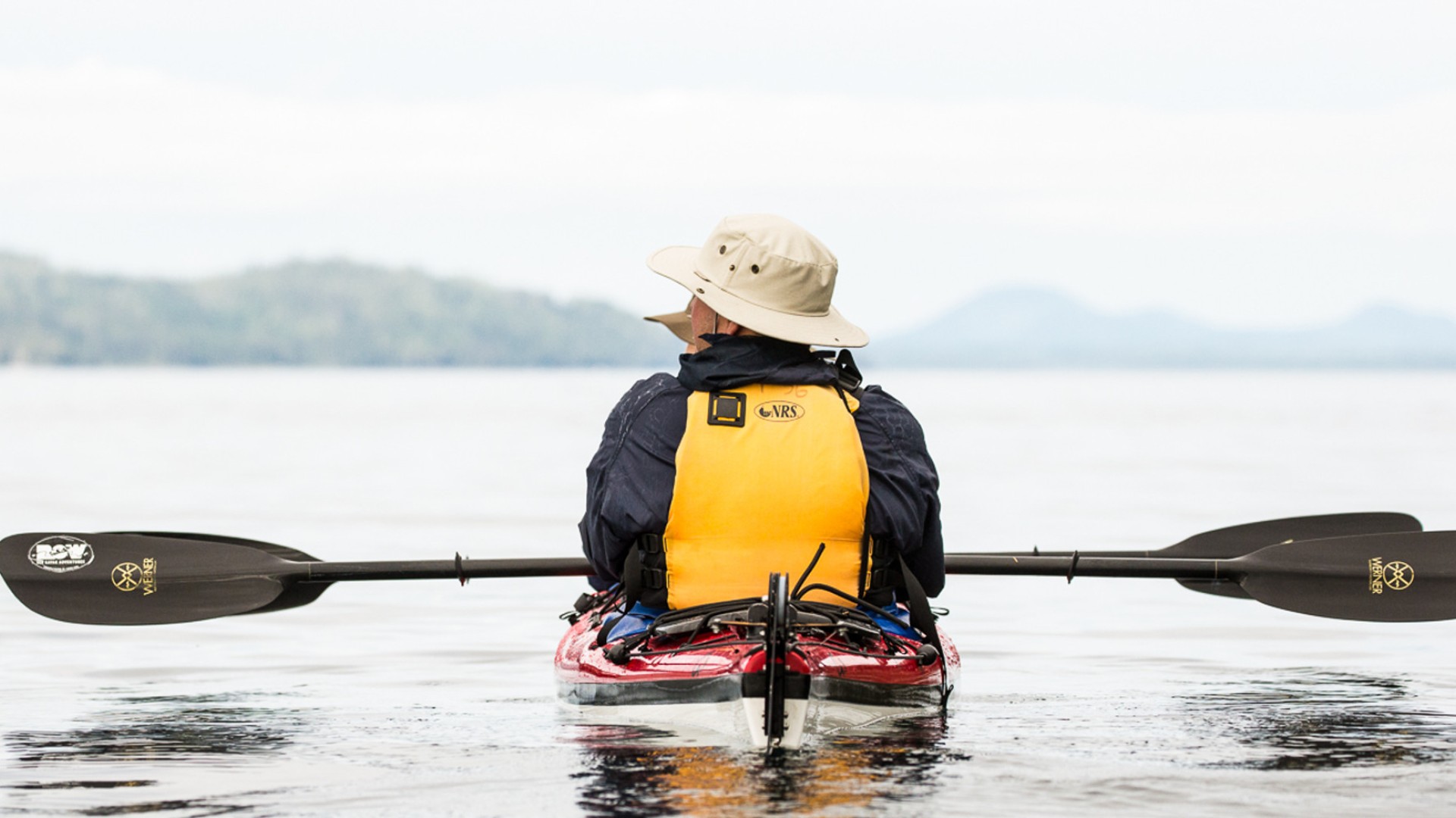 Person looking out onto the ocean while in a sea kayak with their paddle across their lap 