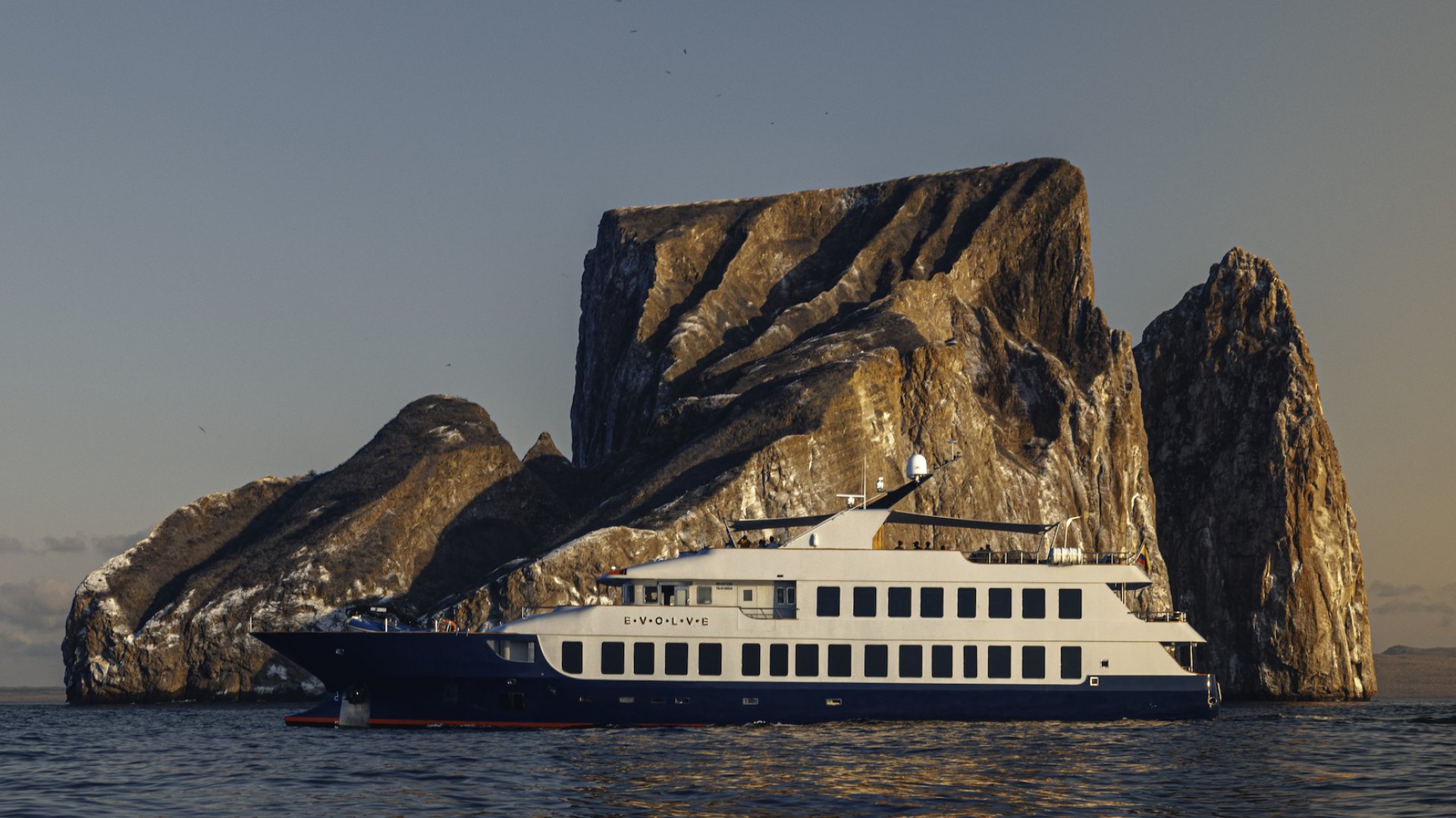 Small ship cruising past Kicker Rock at sunset in the Galapagos