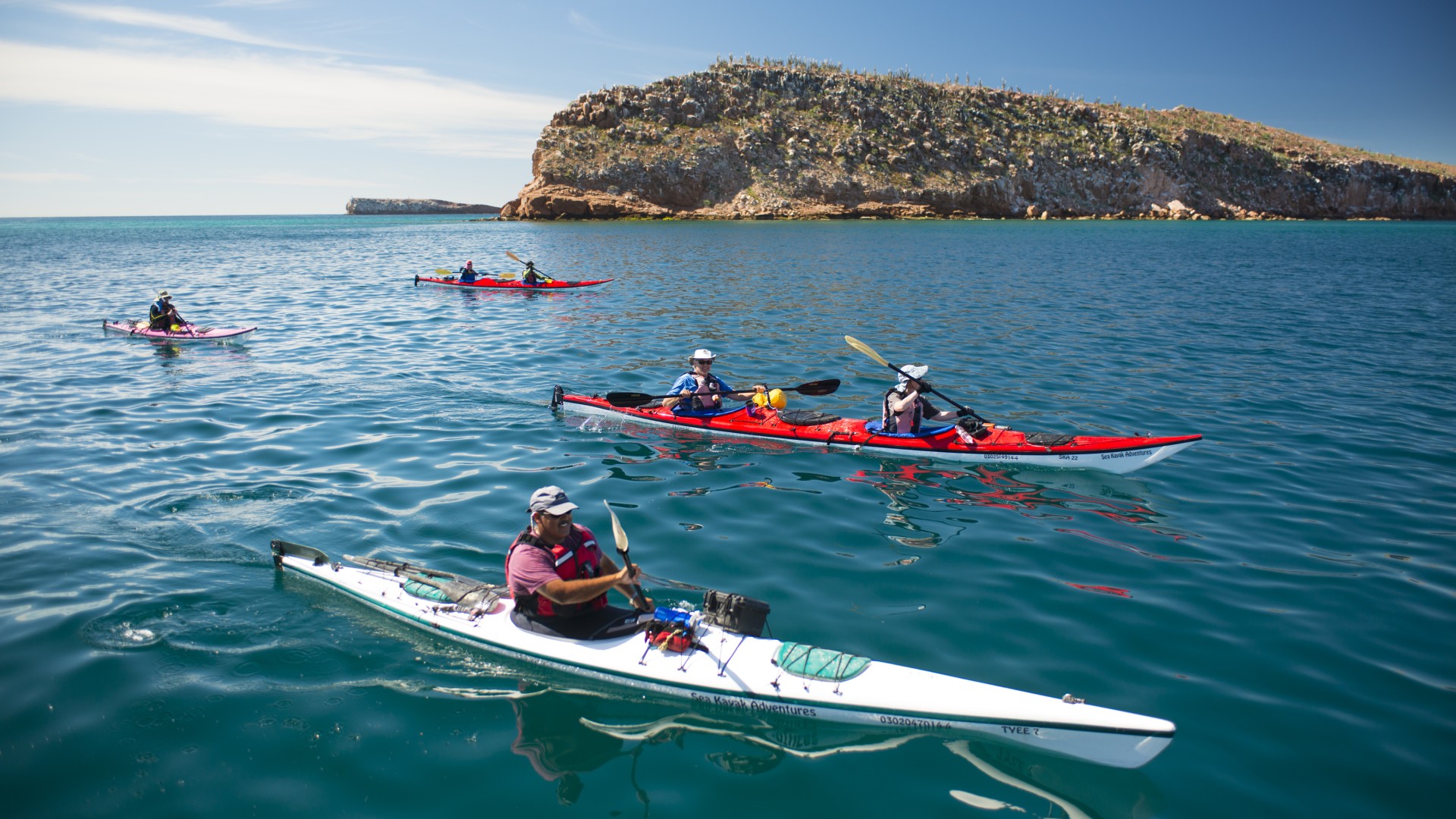 Kayakers smiling at the camera as they paddle down the Baja California Sur peninsula on the Gulf of California on a sunny day