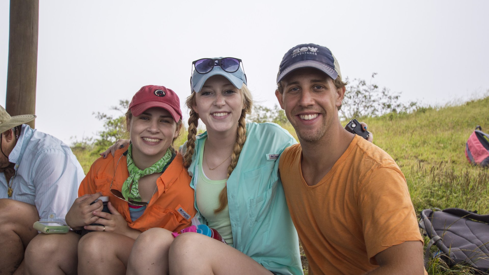 A man on the right and two women on the left smiling for a photo in a grassy field in the Galapagos on a foggy day