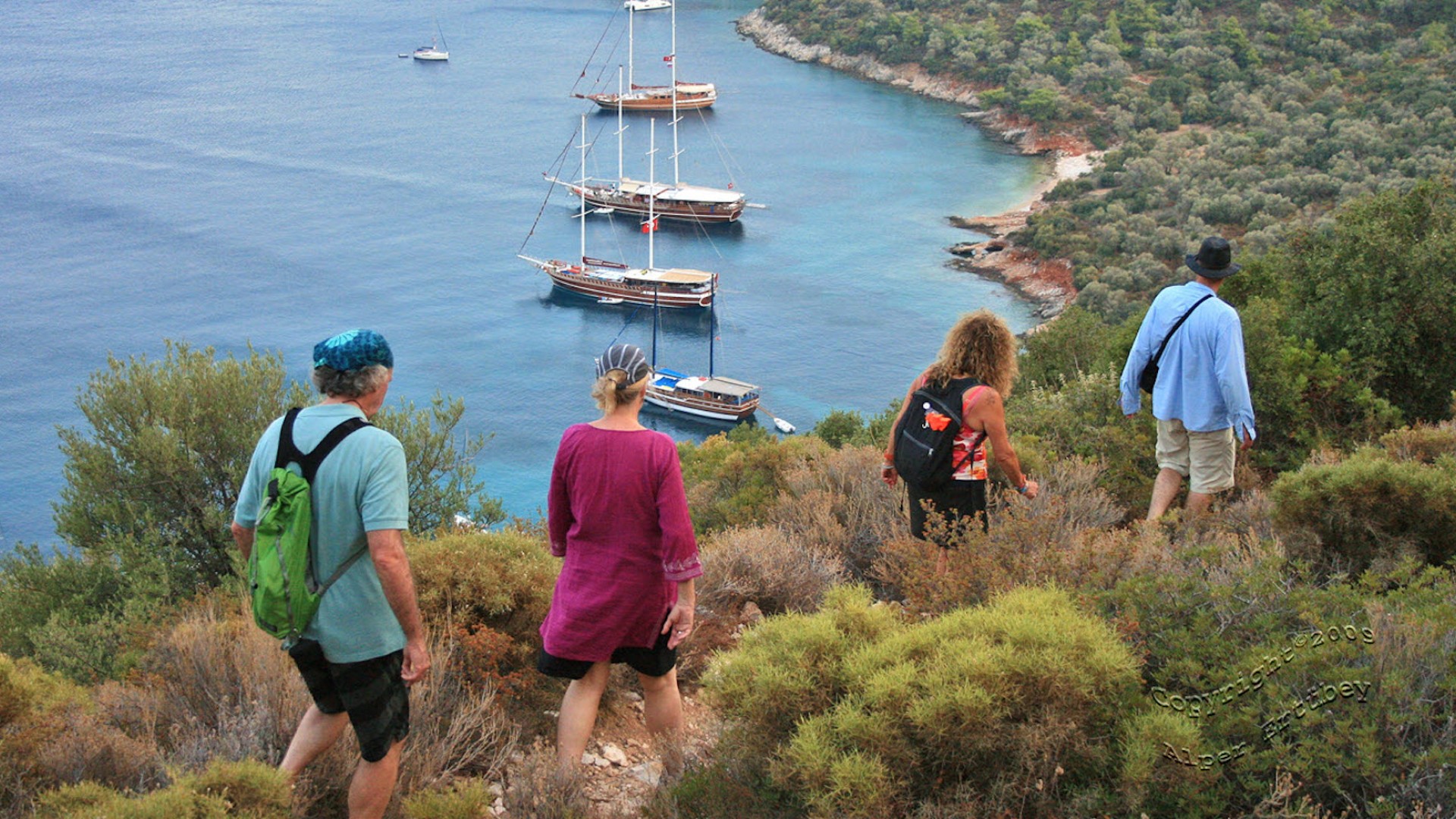 Four people walking across a ridge-line overlooking the sea full of yachts and boats in Turkey