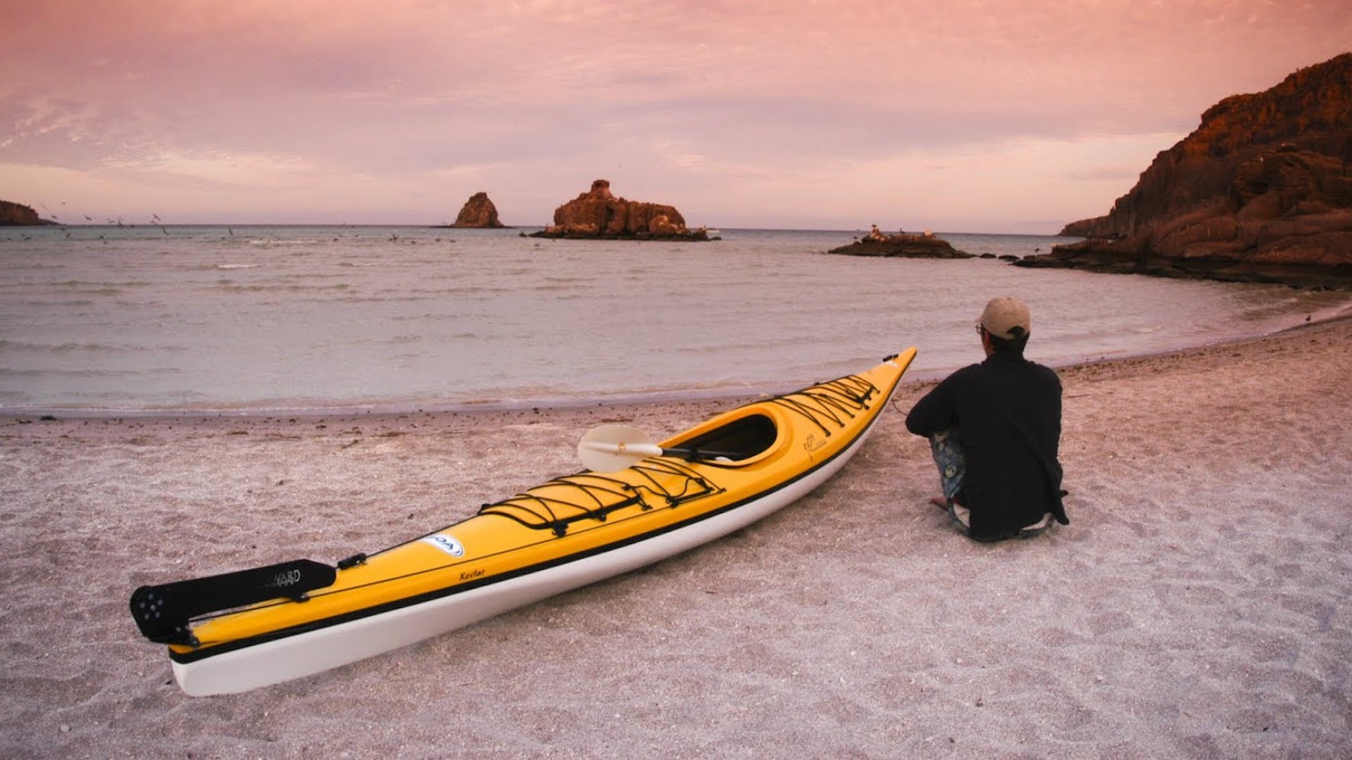 Person sitting next to a single yellow kayak pulled on the shore enjoying the beach in Baja California Sur