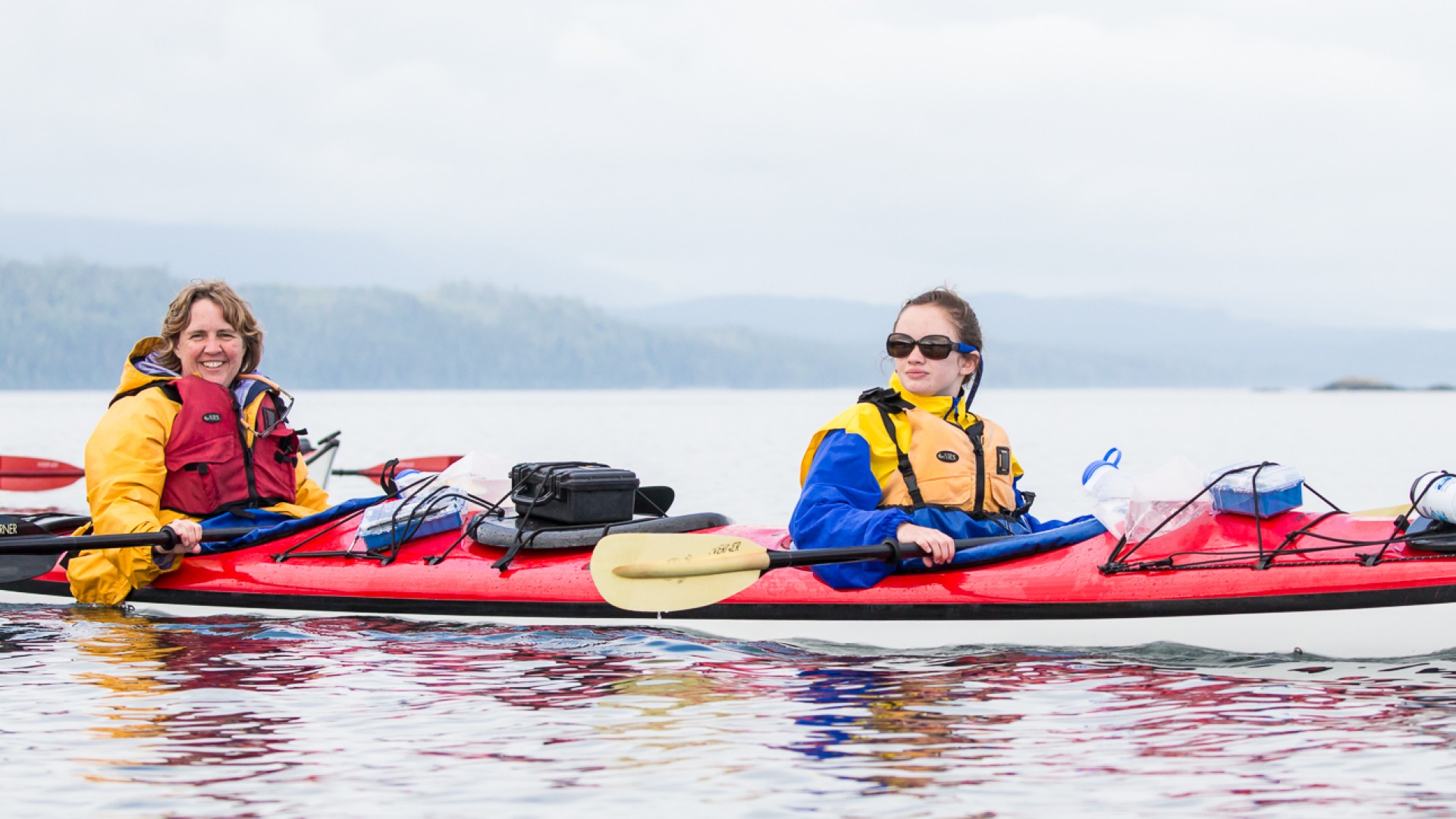 Two women in a red sea kayak on still water in the Johnstone Strait on a cloudy day