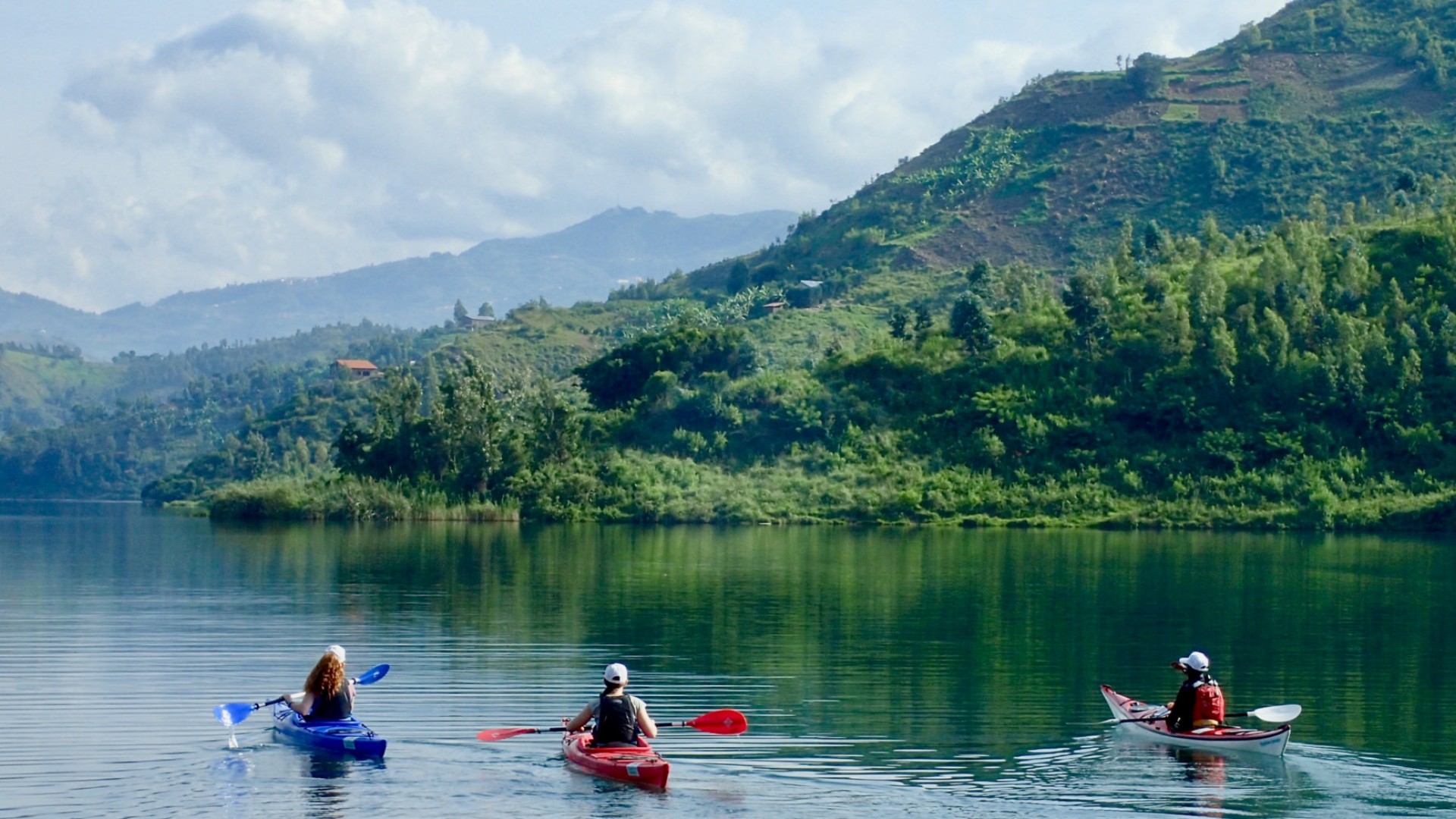 Three people kayaking on Lake Kivu surrounded my lush green rolling hills in rwanda