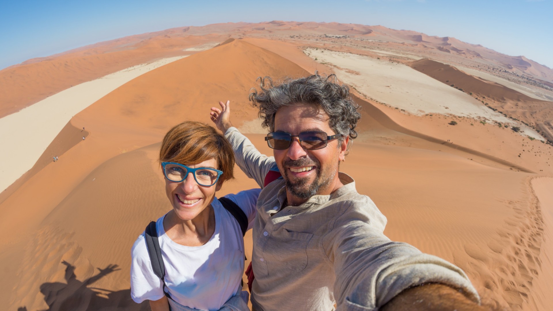 A tourist couple standing on top of a sand dune taking a selfie in the Namib desert