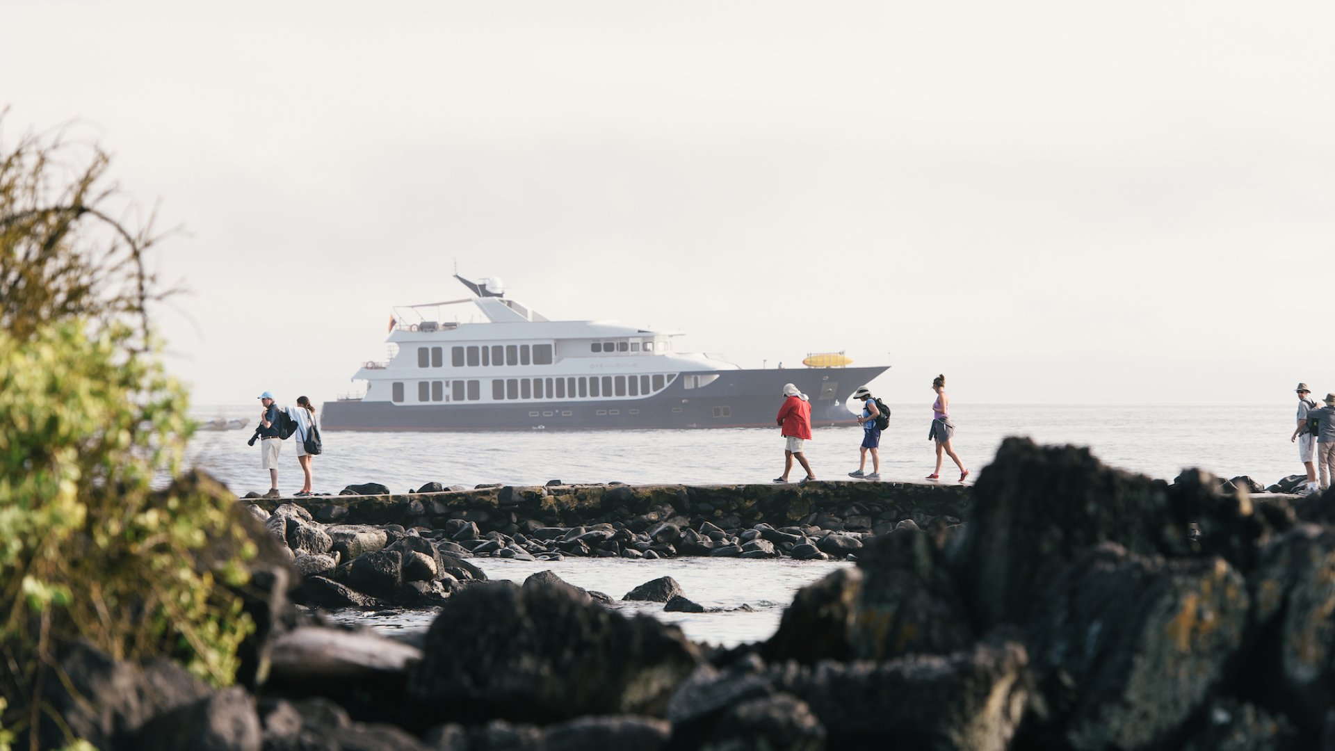 People walking across a bay of rocks along the beach with the Origin cruise ship in the background in the Galapagos Islands Archipelago