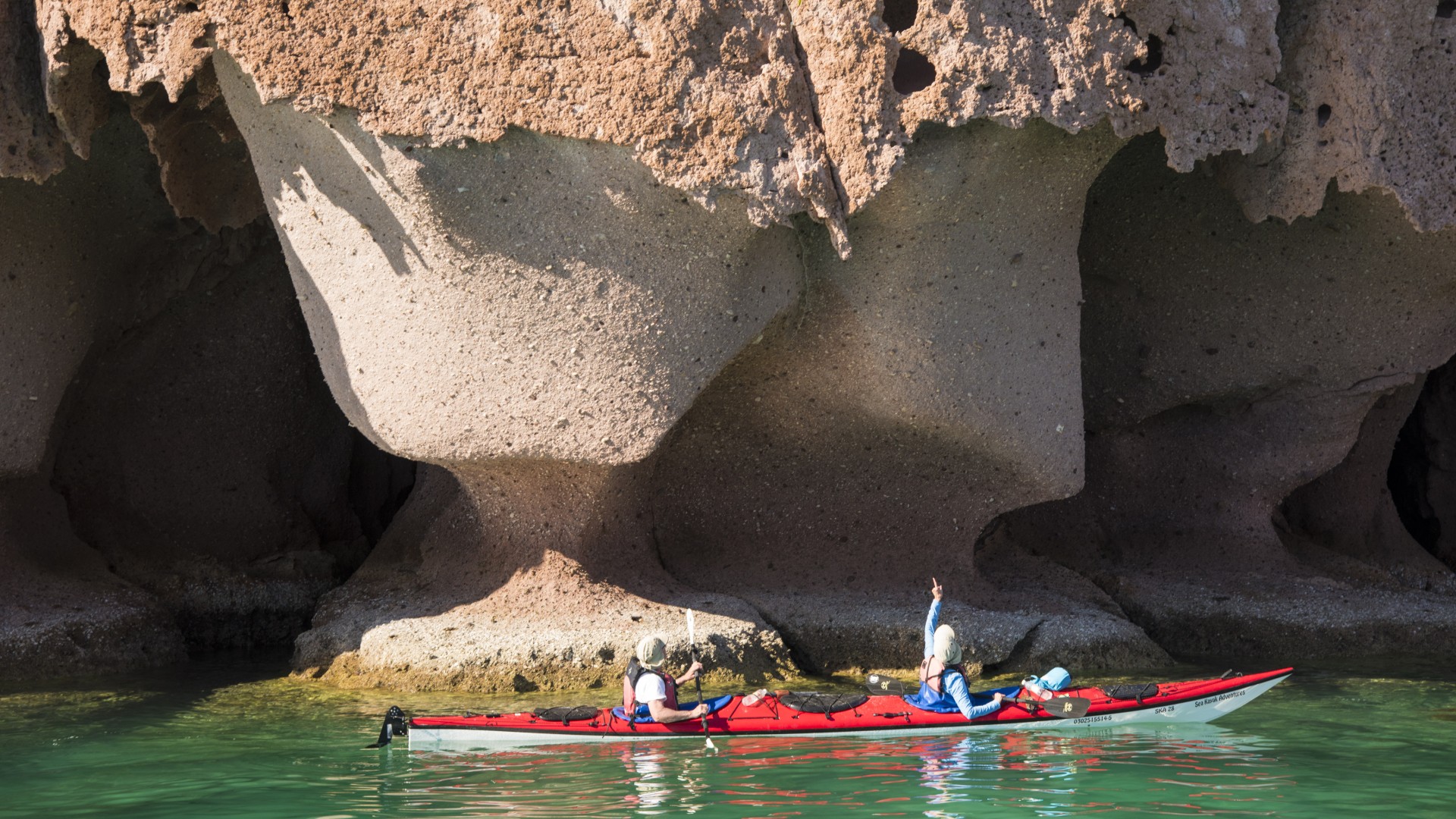 Sea kayakers admiring a large sandstone cliff behind them off the coast of La Paz in Baja California Sur