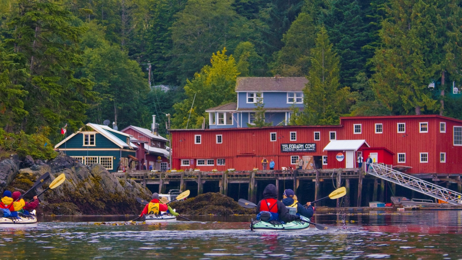 Sea kayakers paddling towards a small and colorful port town in British Columbia