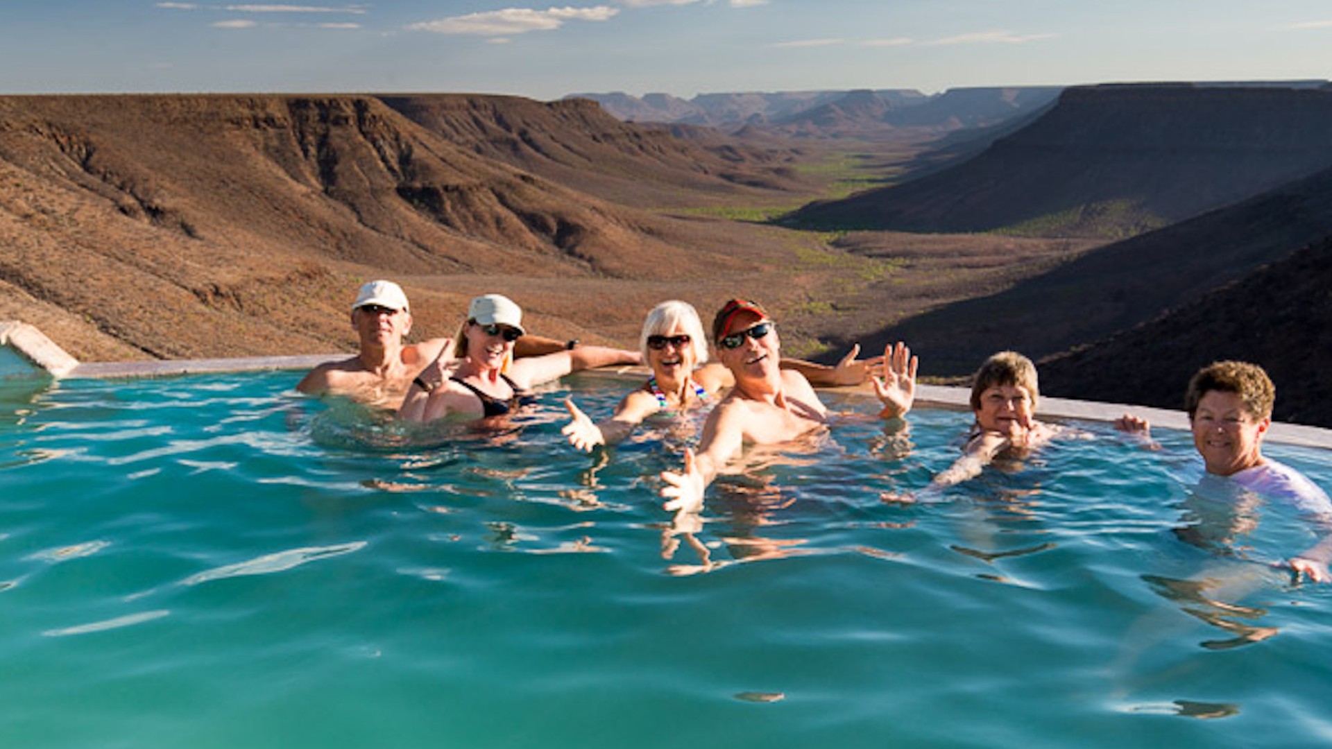 People smiling in a pool overlooking a vast valley in Namibia