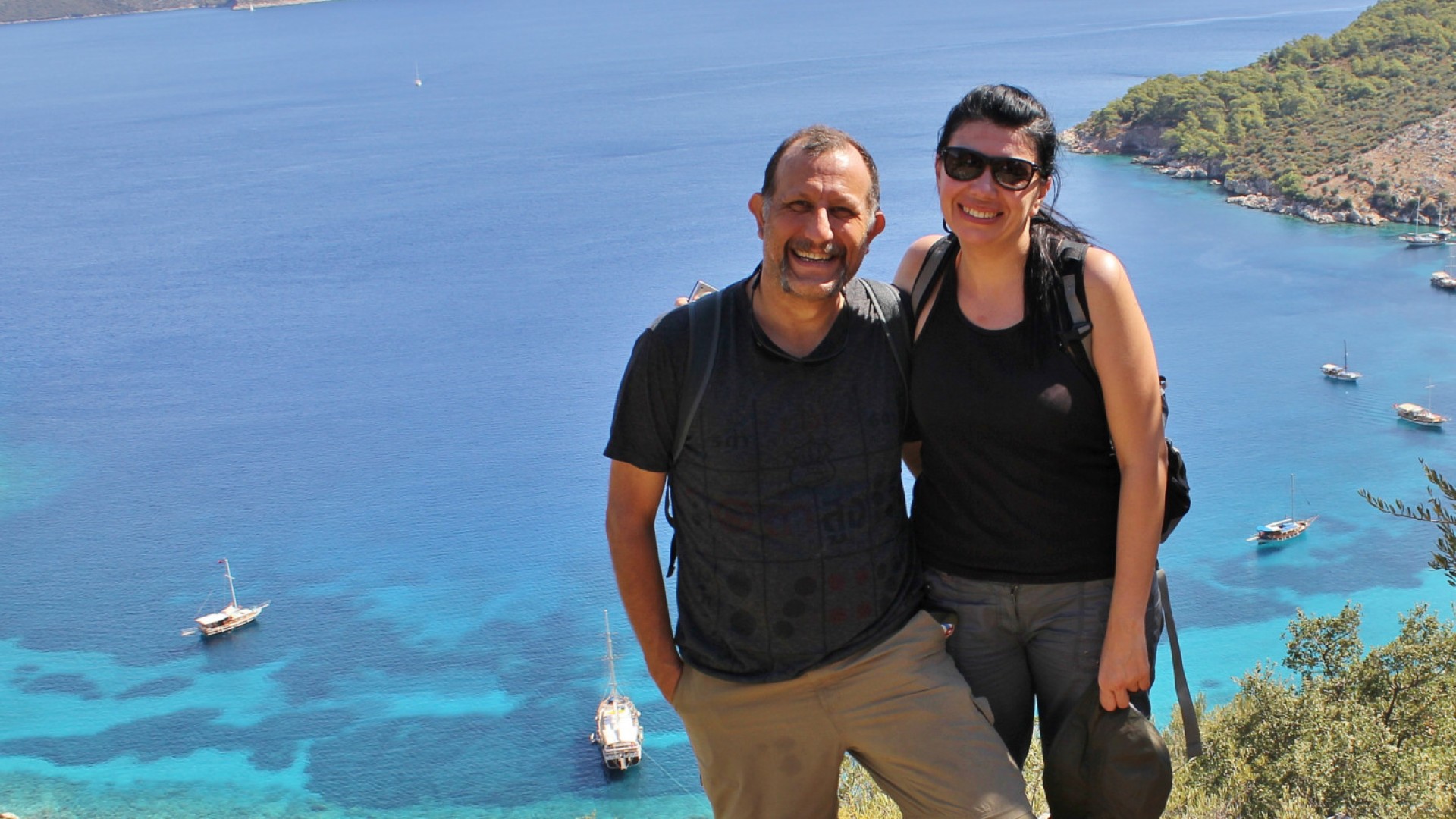 A couple smiling on top of a hike overlooking the Carian Sea behind them in Turkey