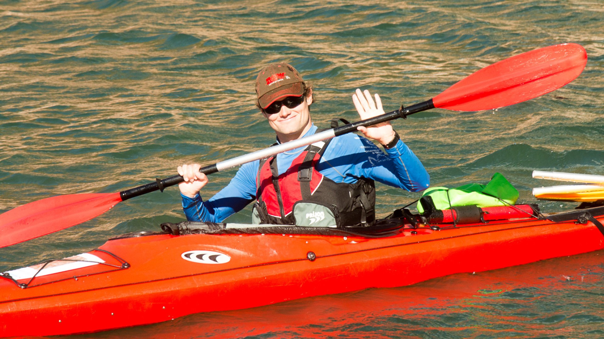 Sea kayaker on the Mediterranean Sea in a red kayak waving while holding their kayak paddle