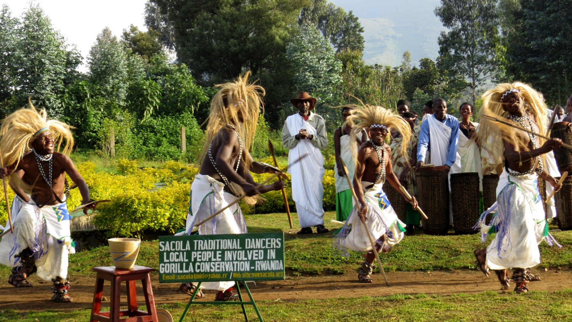 Group of people in Rwanda wearing big head pieces and white sarongs around their waists dancing all together 