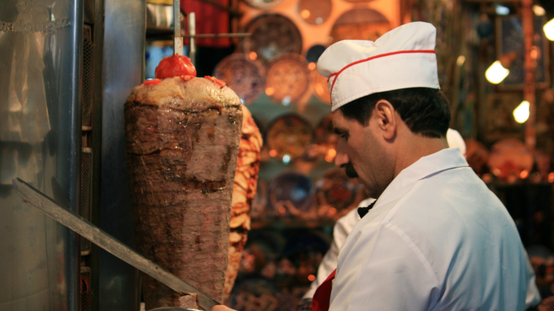 A man in a white chef hat slicing meet of a rotating cooker in Turkey