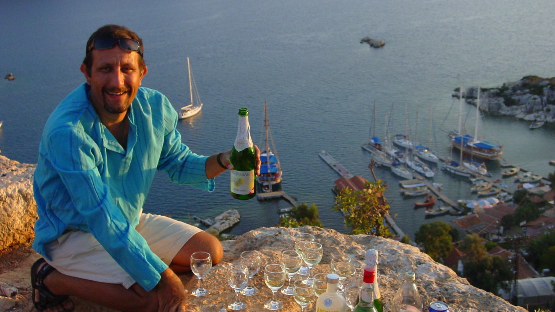 Turkish tour guide at the top of a hike overlooking the water with boats in it serving wine to guests
