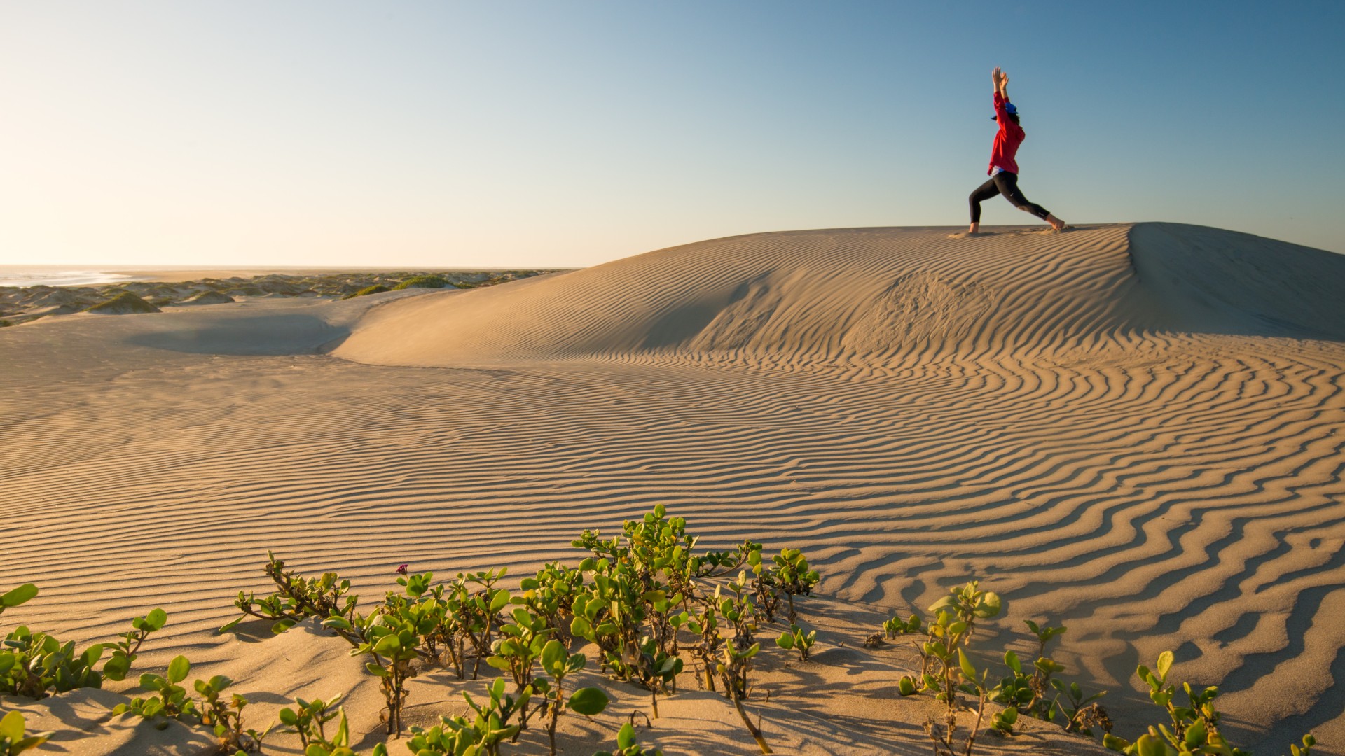 Person doing yoga in the sand dunes of Magdalena Bay during golden hour