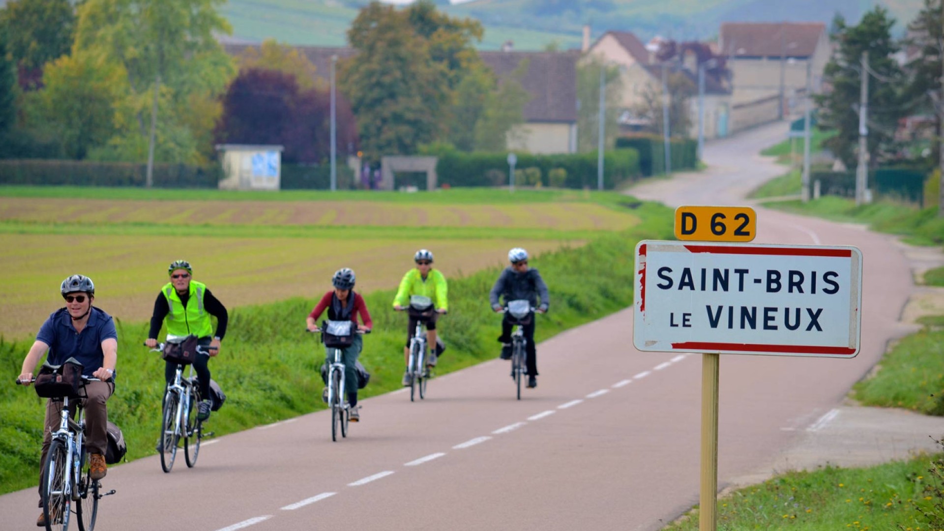 A group of bikers cycling towards the camera on a paved road in the French countryside