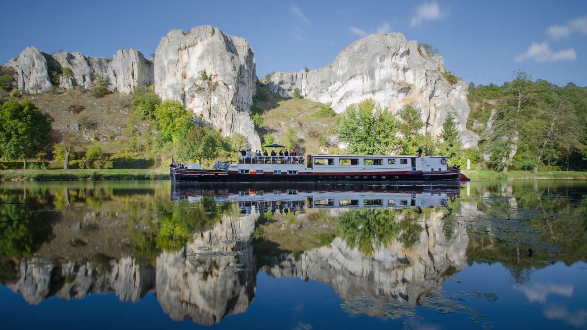 Classic French canal boat gliding past limestone cliffs and reflected on still waters, perfect for those Touring Sites in France.