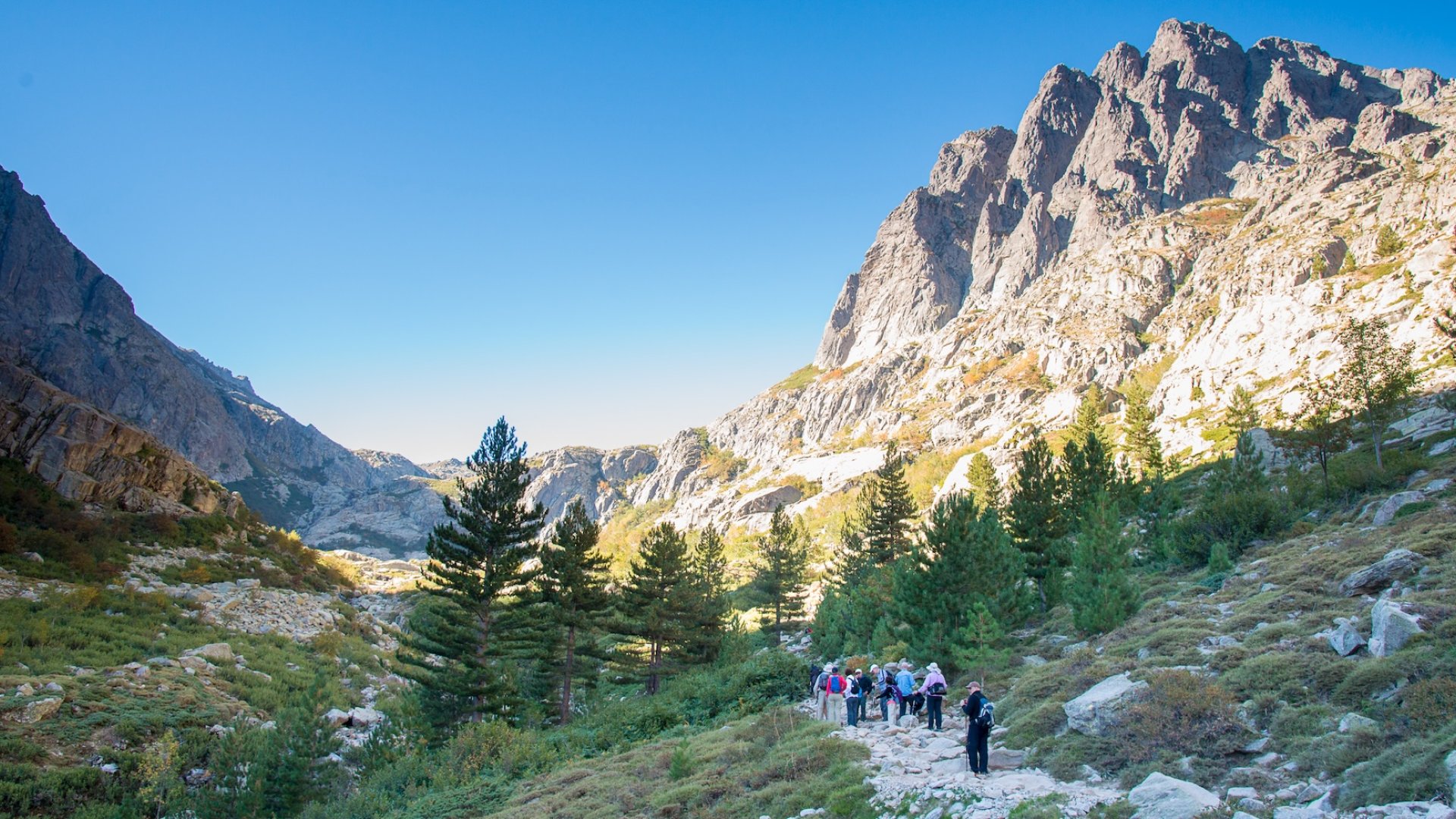 Group of hikers trekking through Corsica’s rugged mountain trails under clear blue skies.