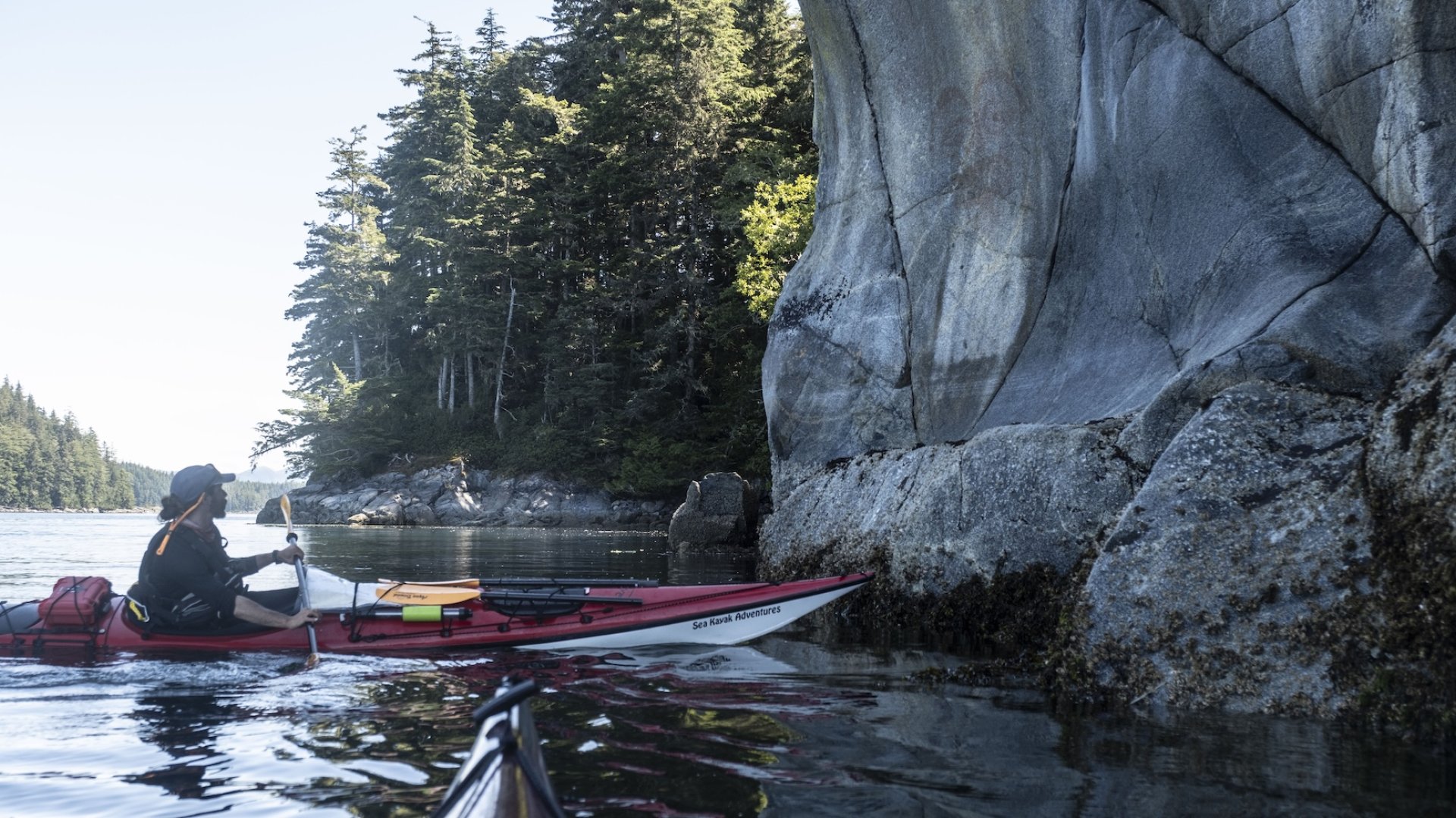 Sea kayaker paddling beside rocky coastal cliffs in British Columbia’s Johnstone Strait