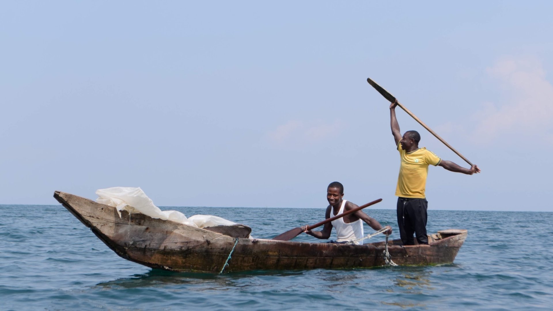 Two fishermen paddling a traditional wooden canoe on Lake Kivu in Rwanda.