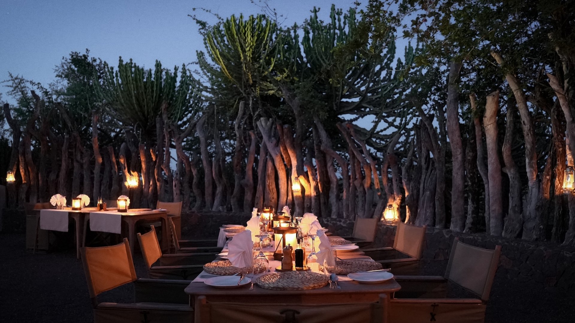 Candlelit outdoor dining setup surrounded by lanterns and wooden fencing in Botswana.