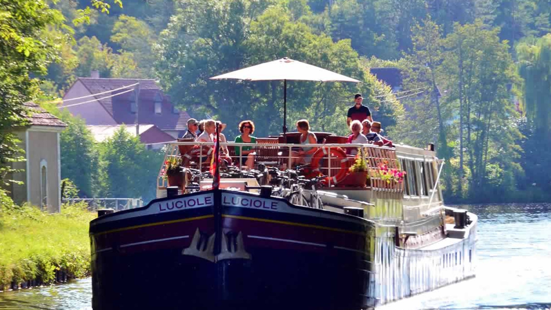 People sitting in circle under an umbrella on the luciole barge on a sunny day in a French canal