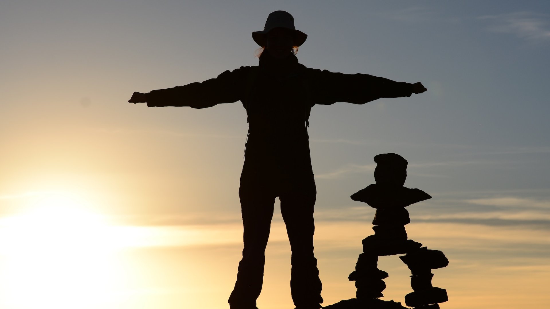 Traveler standing with arms outstretched at sunrise next to stone cairn in Peru – South America travel adventure
