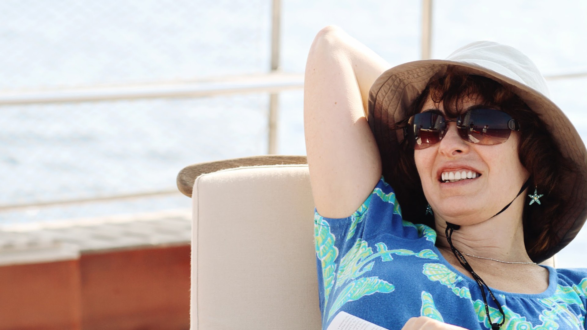 Women wearing sunglasses and a sun hat with her hands behind her head relaxing on a sun chair on a small yacht in Europe