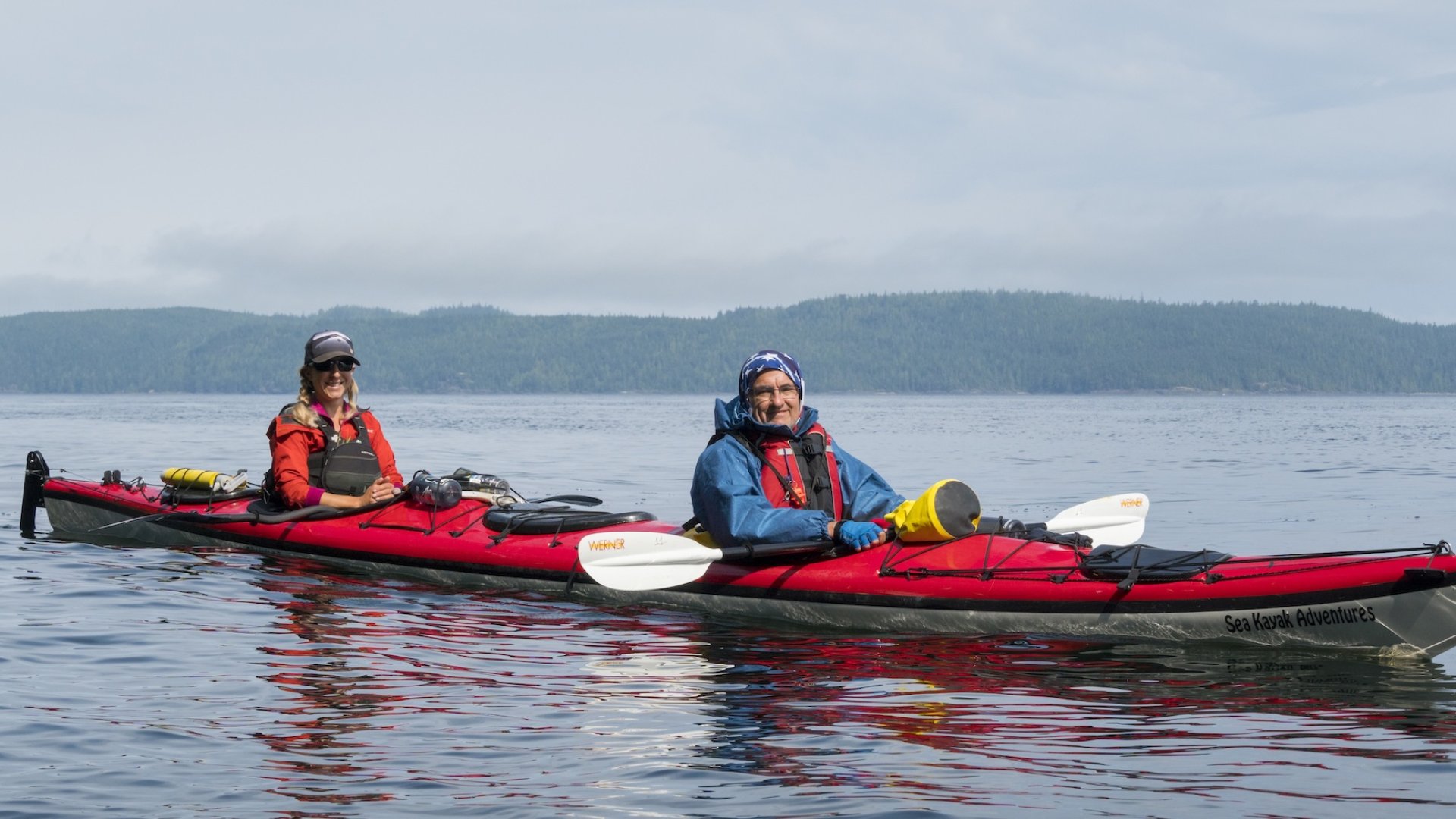 Two sea kayakers smiling while in calm waters off the shores of British Columbia.