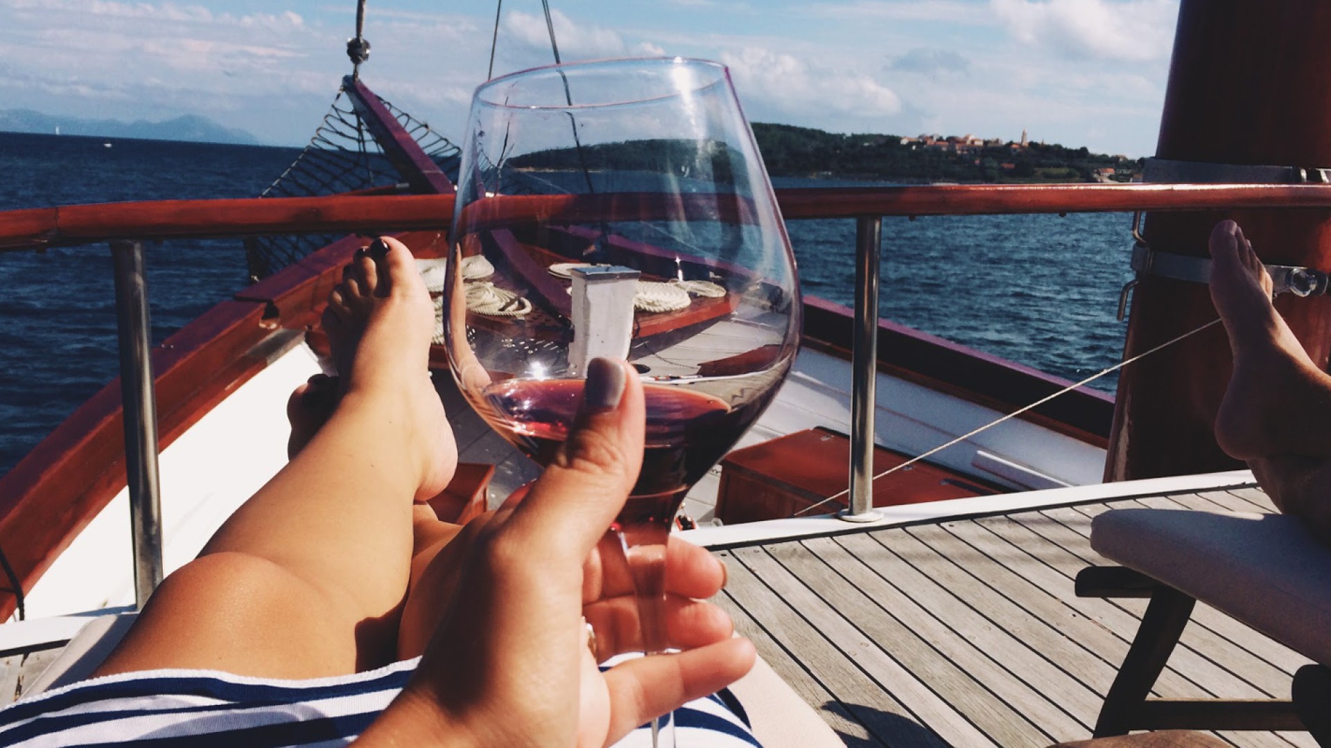 Person reaching out their glass of red wine to cheers while cruising on a small yacht in Croatia on the Mediterranean Sea