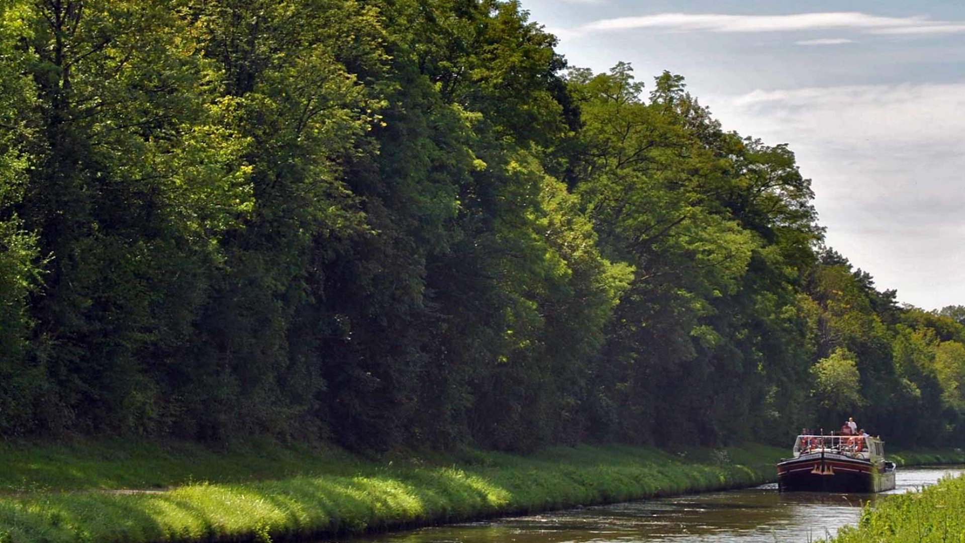 Scenic view of a canal boat cruising through lush green countryside on a sunny day – a peaceful escape for those exploring Canal Boat Tours France.